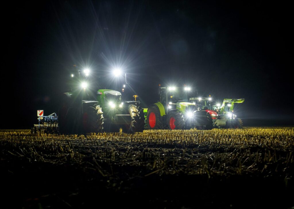 Rząd traktorów z mocnymi lampami roboczymi LED oświetlających pole w nocy