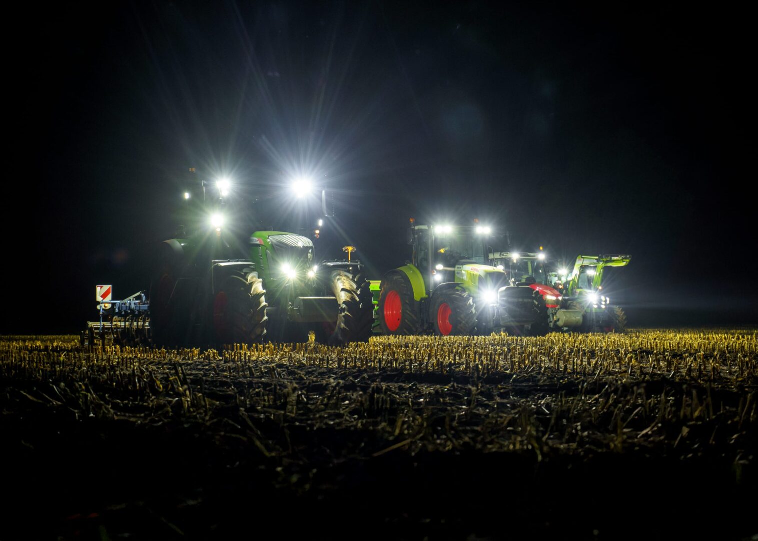 Rząd traktorów z mocnymi lampami roboczymi LED oświetlających pole w nocy